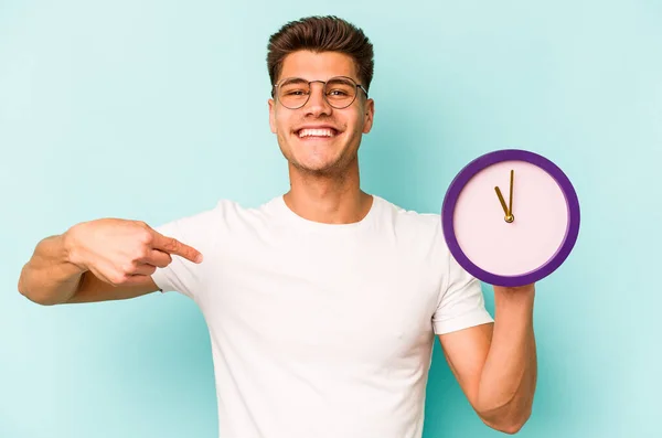 Young Caucasian Man Holding Clock Isolated Blue Background Person Pointing — Fotografie, imagine de stoc