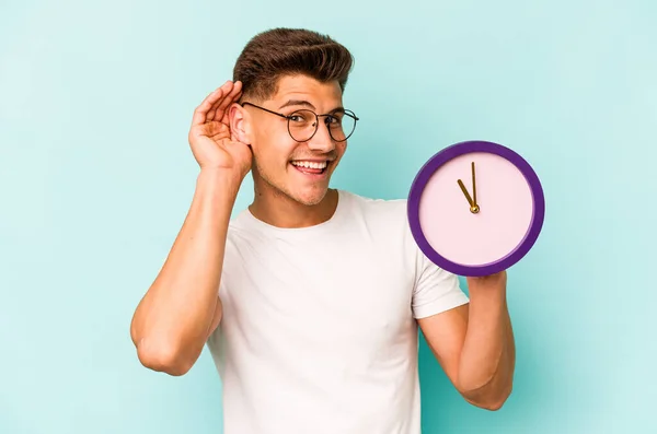 Young Caucasian Man Holding Clock Isolated Blue Background Trying Listening — Foto de Stock