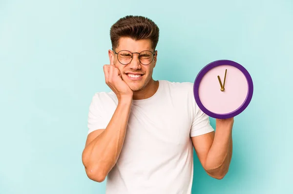 Young Caucasian Man Holding Clock Isolated Blue Background Covering Ears — Stock Photo, Image