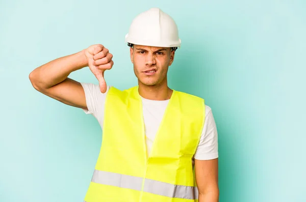 年轻的工人阶级男子被隔离在蓝色背景下 表现出不喜欢的姿态 大拇指垂下 不同意的概念 — 图库照片