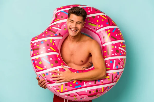 Mavi arka planda izole edilmiş şişme bir çörek tutan genç beyaz adam gülüyor ve eğleniyor..