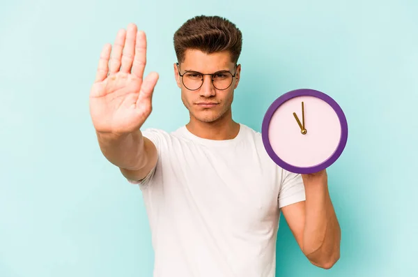 Junger Kaukasischer Mann Hält Eine Auf Blauem Hintergrund Isolierte Uhr — Stockfoto