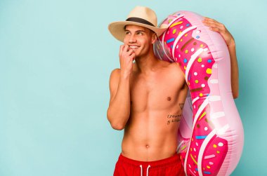 Mavi arka planda izole edilmiş şişirilebilir donut tutan genç beyaz adam bir şeyin fotokopi odasına baktığını düşünerek rahatladı..