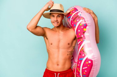 Mavi arka planda izole edilmiş şişirilebilir donut tutan genç beyaz adam şok oldu, o önemli bir toplantı hatırladı.