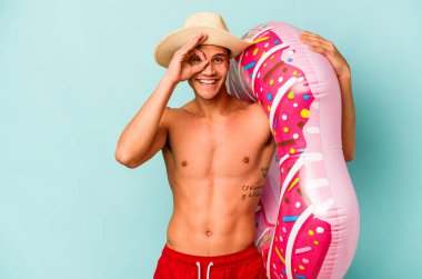 Mavi arka planda izole edilmiş şişirilebilir donut tutan genç beyaz bir adam heyecanlı..