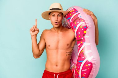 Mavi arka planda izole edilmiş şişirilebilir donut tutan genç beyaz bir adam harika bir fikre, yaratıcılık kavramına sahip..