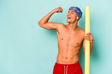 Beyaz tenli genç yüzücü elinde köpük çubukla mavi arka planda izole bir şekilde zafer kazandıktan sonra yumruğunu kaldırıyor..