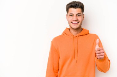 Beyaz arka planda izole edilmiş genç beyaz adam gülümsüyor ve başparmağını kaldırıyor.