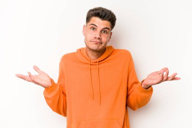 Beyaz arka planda izole edilmiş genç beyaz bir adam sorgulama sırasında omuz silkiyor ve şüphe duyuyor..