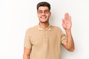 Beyaz arka planda izole edilmiş genç beyaz bir adam gülümseyerek beş numarayı parmaklarıyla gösteriyor..