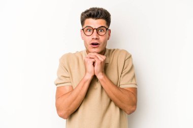 Beyaz arka planda izole edilmiş genç beyaz bir adam şans için dua ediyor, şaşırmış ve ağzını açıp önüne bakıyor..