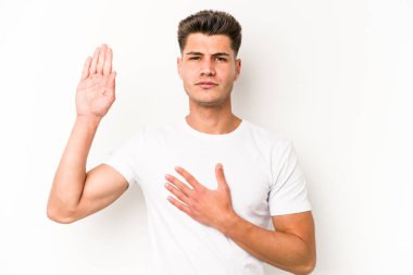 Beyaz arka planda izole edilmiş genç beyaz adam yemin ediyor, elini göğsüne koyuyor..