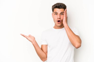 Beyaz arka planda izole edilmiş genç beyaz adam, avuç içi fotokopi alanını elinde tutmaktan etkilenmiş..