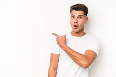 Beyaz arka planda izole edilmiş genç beyaz bir adam gülümsüyor ve boş alanda bir şeyler gösteriyor..