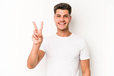 Beyaz arka planda izole edilmiş genç beyaz bir adam zafer işareti gösteriyor ve gülümsüyor..