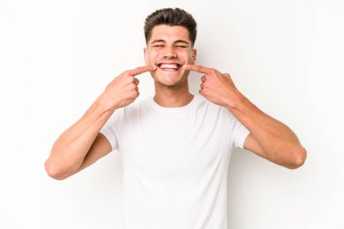 Beyaz arka planda izole edilmiş genç beyaz adam gülümsüyor, parmaklarını ağıza doğrultuyor..