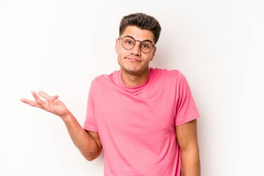 Beyaz arka planda izole edilmiş genç beyaz bir adam sorgulama sırasında omuz silkiyor ve şüphe duyuyor..