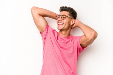 Beyaz arka planda izole olmuş genç beyaz bir adam kendini güvende hissediyor, elleri başının arkasında..