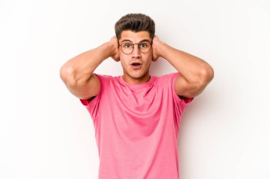 Beyaz arka planda izole edilmiş genç beyaz bir adam kulakları kulaklarıyla kapatıyor ve çok ses duymamaya çalışıyor..