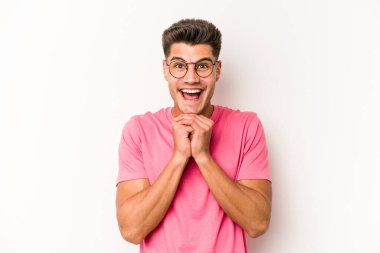 Beyaz arka planda izole edilmiş genç beyaz bir adam şans için dua ediyor, şaşırmış ve ağzını açıp önüne bakıyor..