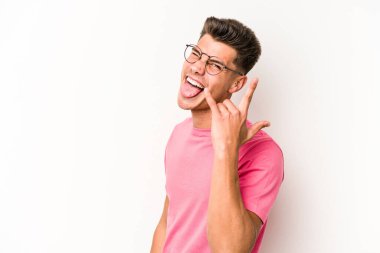 Beyaz arka planda izole edilmiş genç beyaz bir adam parmaklarıyla kaya hareketi gösteriyor.