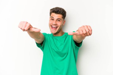 Beyaz arka planda izole edilmiş genç beyaz bir adam iki parmağını da kaldırıyor, gülümsüyor ve kendinden emin..