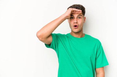 Beyaz arka planda izole edilmiş genç beyaz bir adam uzaklara bakıyor ve elini alnına koyuyor..