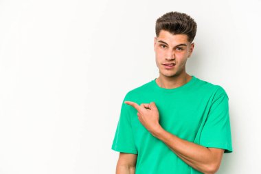 Beyaz arka planda izole edilmiş genç beyaz bir adam gülümsüyor ve boş alanda bir şeyler gösteriyor..
