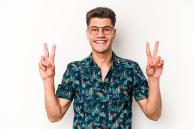 Beyaz arka planda izole edilmiş genç beyaz bir adam zafer işareti gösteriyor ve gülümsüyor..