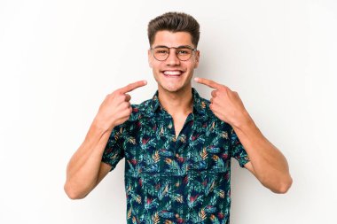 Beyaz arka planda izole edilmiş genç beyaz adam gülümsüyor, parmaklarını ağıza doğrultuyor..