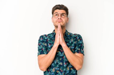 Beyaz arka planda izole edilmiş genç beyaz bir adam el ele tutuşup, ağız kenarında dua ediyor, kendinden emin..