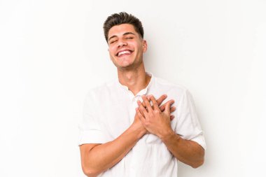 Beyaz arka planda soyutlanmış beyaz tenli genç bir adam gülüyor, elini yüreğine koyuyor, mutluluk kavramını koruyor..