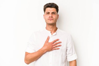 Beyaz arka planda izole edilmiş genç beyaz adam yemin ediyor, elini göğsüne koyuyor..