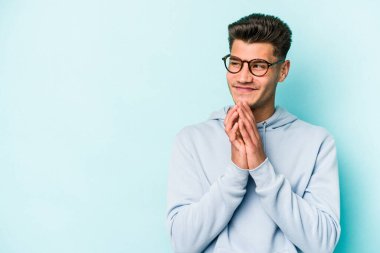 Kafkasyalı genç bir adam mavi arka planda izole edildi. Aklında bir plan kuruyor, bir fikir kuruyor..