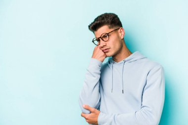 Mavi arka planda izole edilmiş, üzgün ve dalgın hisseden, kopyalama alanına bakan genç beyaz bir adam..