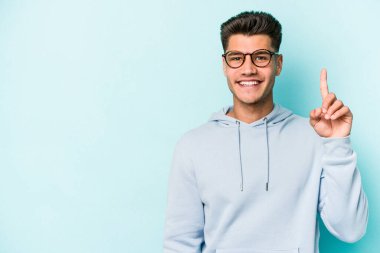 Mavi arka planda izole edilmiş genç beyaz adam bir numarayı parmağıyla gösteriyor..