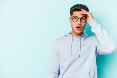 Mavi arka planda izole edilmiş genç beyaz adam yüksek sesle bağırıyor, gözleri açık ve elleri gergin tutuyor..