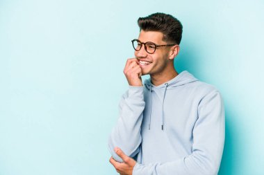 Mavi arka planda izole edilmiş genç beyaz adam rahatlamış bir şeyin fotokopi odasına baktığını düşünüyor..