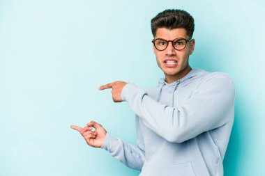 Mavi arka planda izole edilmiş genç beyaz adam işaret parmağıyla fotokopi alanını işaret ederek şok oldu..