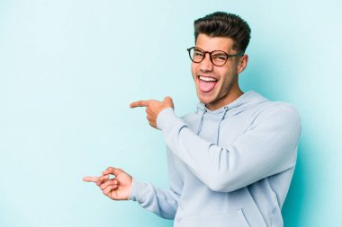 Mavi arka planda izole edilmiş genç beyaz adam işaret parmağıyla fotokopi alanını işaret ederek heyecan ve arzusunu ifade ediyor..