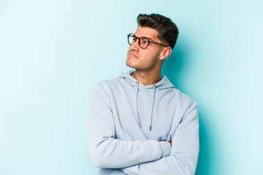 Kafkasyalı genç adam mavi arka planda izole edilmiş hedeflerine ve amaçlarına ulaşma hayali kuruyor.