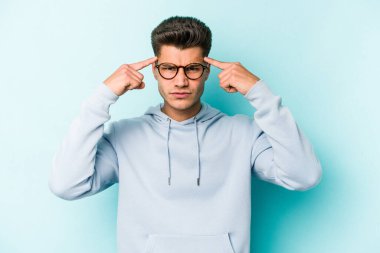 Kafkasyalı genç adam mavi arka planda izole edilmiş bir göreve odaklanmış, parmaklarını işaret ediyor..