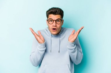 Kafkasyalı genç adam mavi arka planda izole edildi. Şaşırdı ve şok oldu..