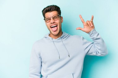 Mavi arka planda izole edilmiş genç beyaz adam boynuzlarını devrim konsepti olarak gösteriyor..