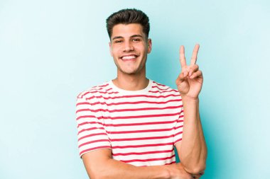 Mavi arka planda izole edilmiş genç beyaz adam iki numarayı parmaklarıyla gösteriyor..