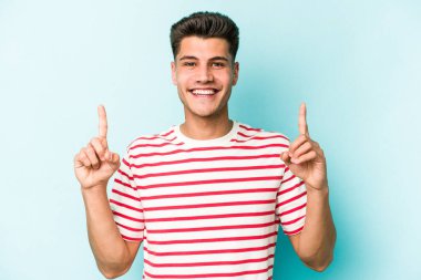 Mavi arka planda izole genç beyaz adam işaret iki ön parmakları boş bir boşluk gösteren.