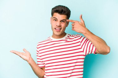 Kafkasyalı genç adam mavi arka planda izole edilmiş ve elinde bir ürün tutuyor..