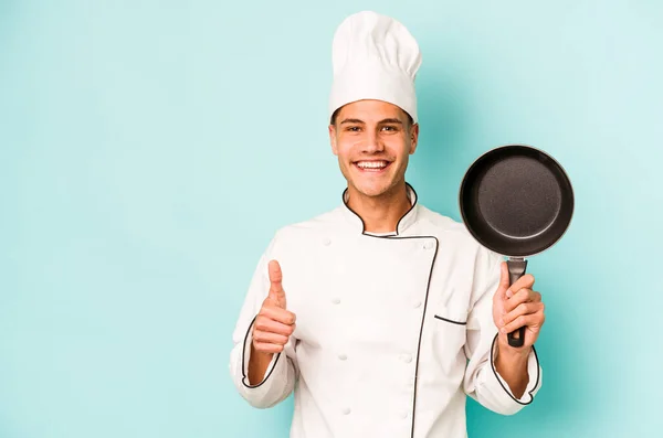 年轻的高加索厨师 拿着被蓝色背景隔离的飞盘 微笑着举起大拇指 — 图库照片