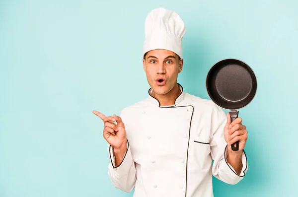 年轻的高加索厨师拿着用蓝色背景隔开的飞盘 指向侧边 — 图库照片