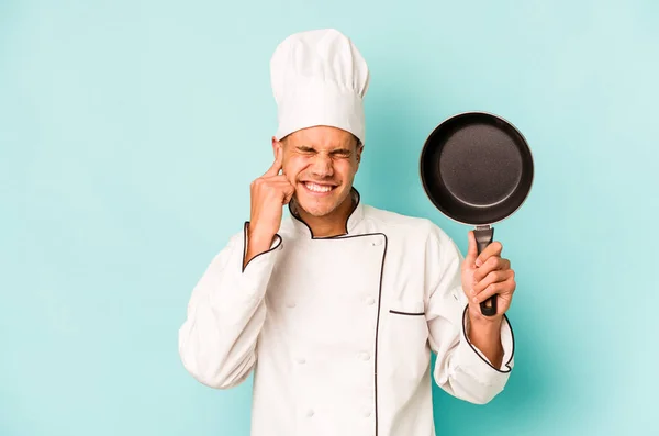 年轻的高加索厨师手拿着用蓝色背景隔离的飞盘 用手捂住耳朵 — 图库照片